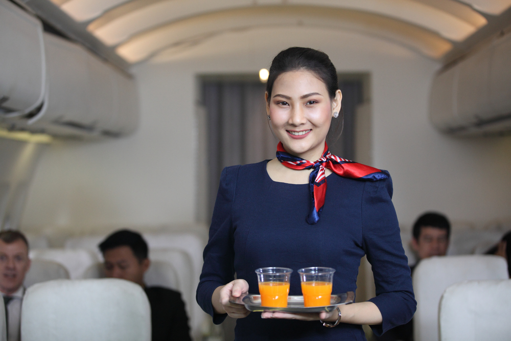 A smiling flight attendant standing while holding a tray of two glasses of orange juice
